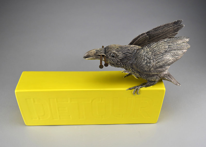 Ceramic sculpture of a crow sitting on a sign that says "Detour"