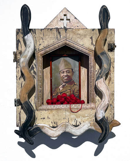 Artwork with carved wooden snakes, photo of soldier and balls of red thread