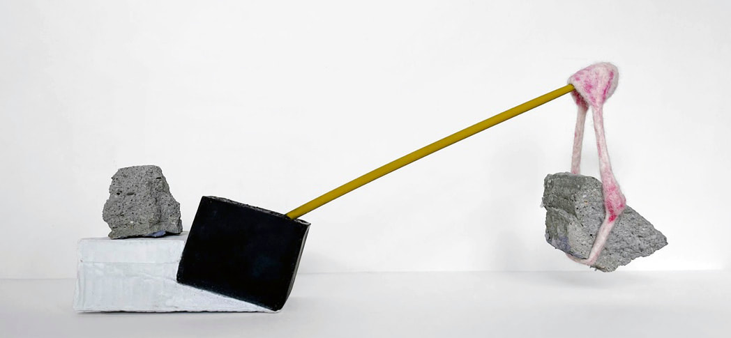sculptural art with three objects together balancing a yellow wood arm with a piece of concrete suspended by yarn