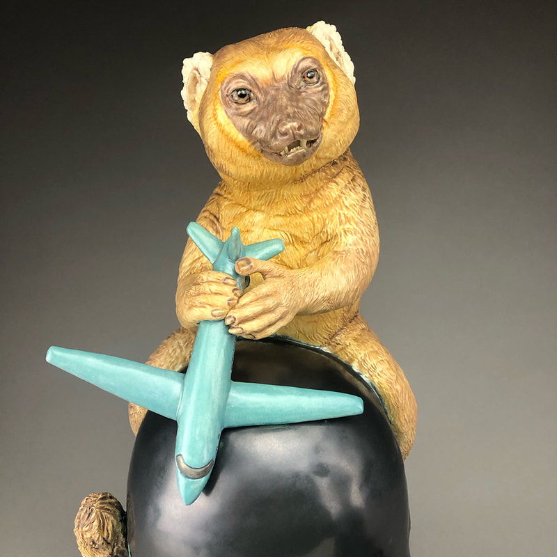 Detail of a ceramic sculpture, showing a King golden lemur holding an airplane.