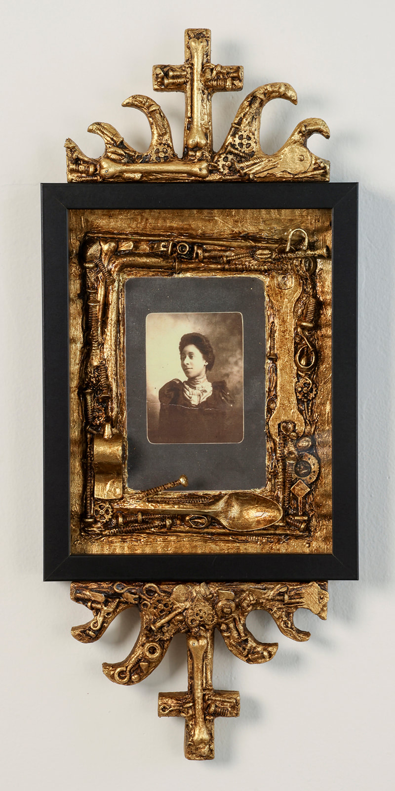 photo portrait of a Black woman in fur in a frame bordered by gold leafed utensils and hardware and with a cross on top