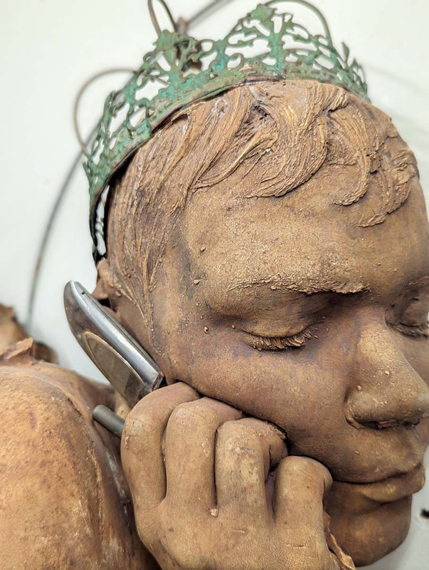 Detail of a bronze sculptural head with hand holding a cellphone