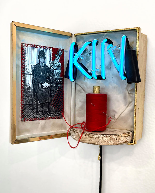 3d Artwork in a jewelry box with a drawing of a oman inside stitched with red thread tied to a spool and with the word "Kin" in neon