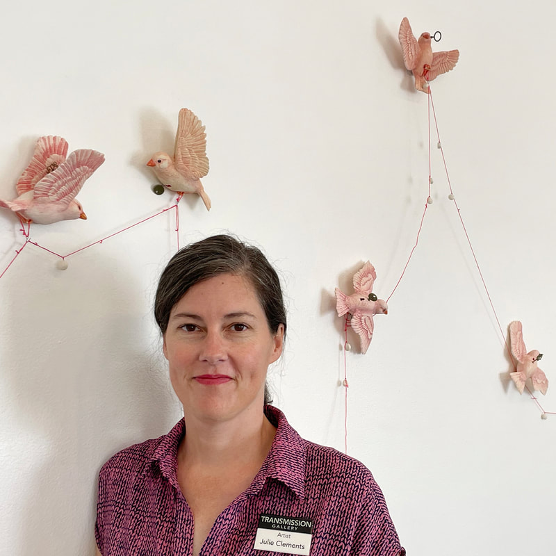 Artist with 20 ceramic canaries with keys and with pills strung on a line between the birds.