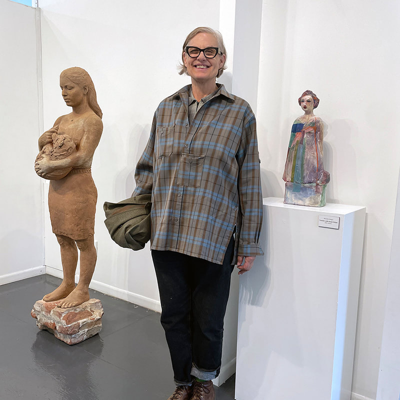 tall woman with large dark glasses standing next to a colorful sculpture of a femail figure