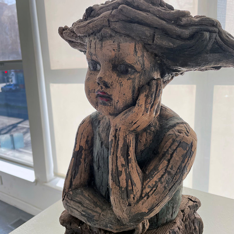 ceramic sculpture of a pensive doll with her hand on her face that looks like carved wood