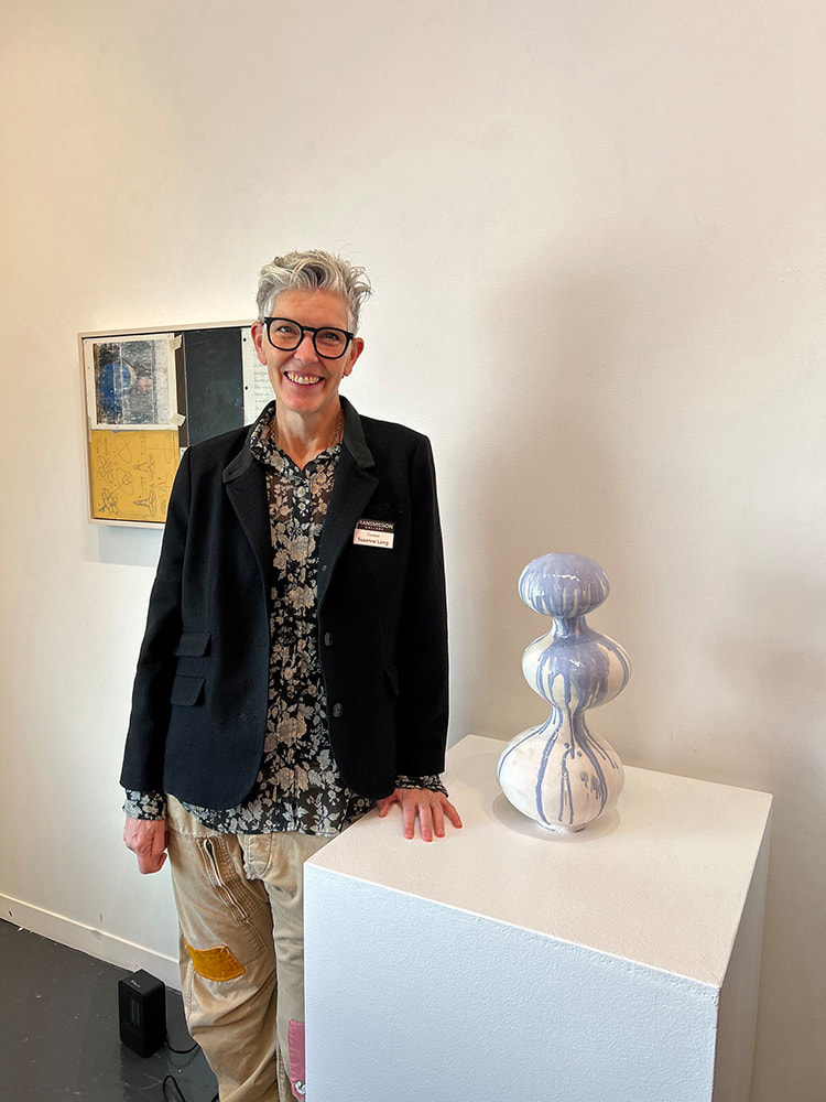 Woman with short hair and big glasses standing next to a sculpture formed by three bulbously shape sections