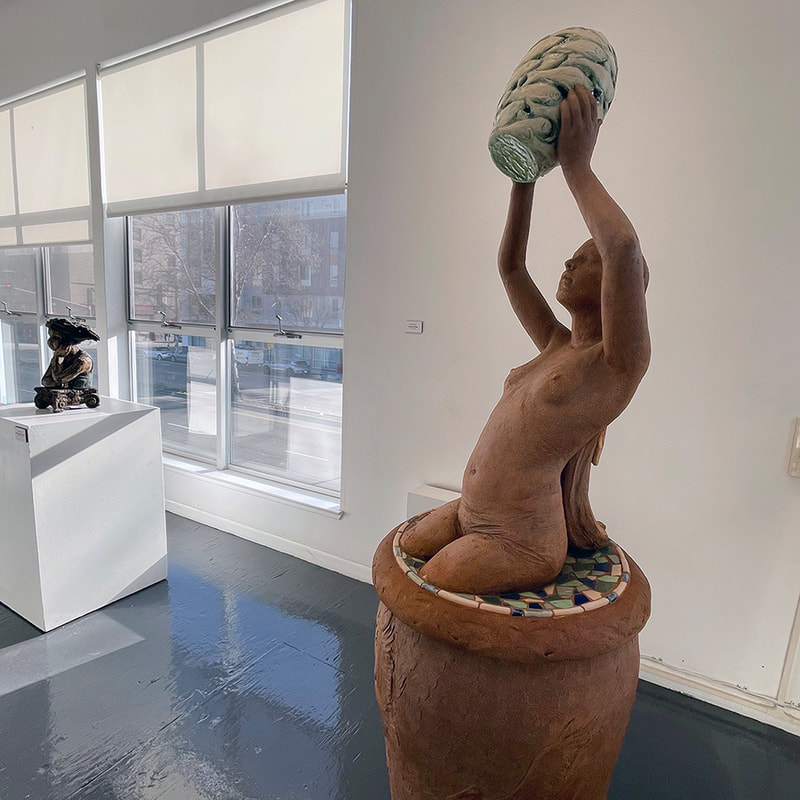 sculpture of a young woman with long hair  holding a vase aloft, the vase is formed from fish shapes