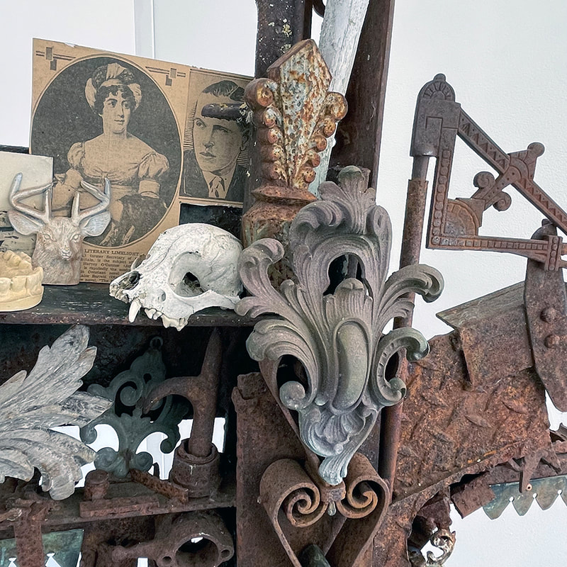 detail of a cross shaped sculpture made of many objects including an animal skull and architectural filigree