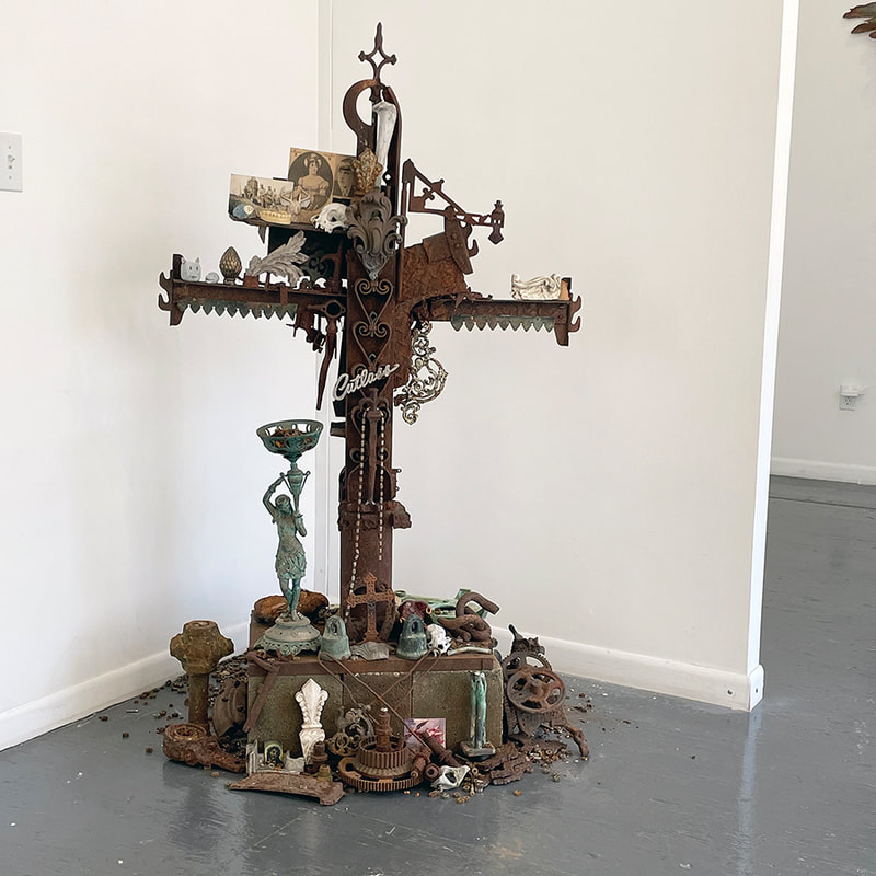 a cross shaped sculpture made of many objects