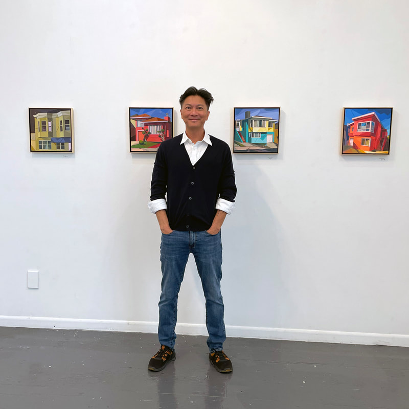 Man wearing a sweater, button up shirt and jeans standing in front of four of his 12 x 12 inch collage artworks in an art gallery
