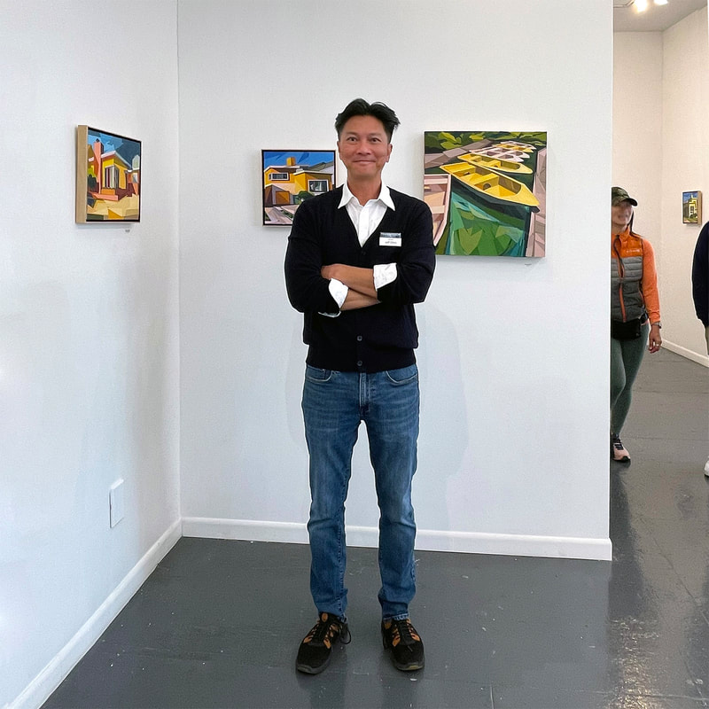 A man wearing a sweater, button up shirt and jeans standing in front of collage artworks in an art gallery