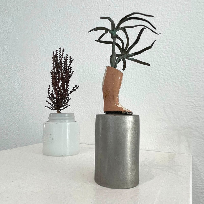 tiny jar with cast metal foliage with doll foot with metal plant on top of mtal cylinder