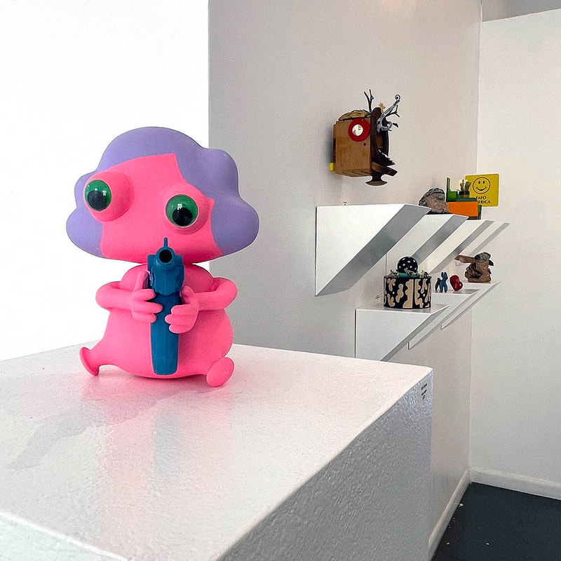Pink girl sculpture with purple hair and toy gun